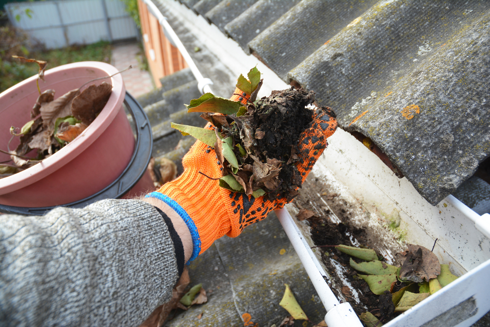 person scooping leaves and dirt out of a gutter